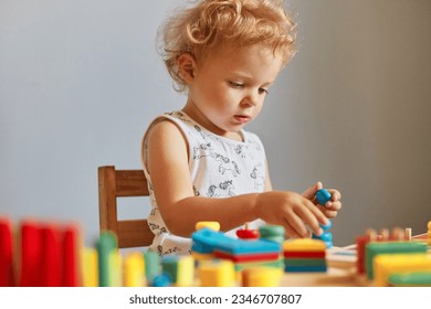 Playground fun and games. Kindergarten's joyful activities. Childhood curiosity and discovery. Concentrated wavy haired blonde infant baby playing wooden educational toys isolated over gray background - Powered by Shutterstock