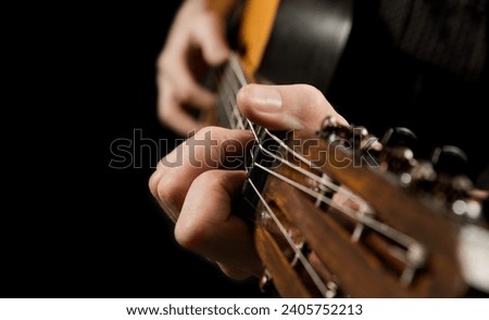 Playing an acoustic guitar on a black background. The musician clamps the frets of the guitar on the neck. Musical instrument in male hands. Close-up. Soft focus.