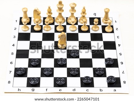playing by different rules on the same board - black checkers and white chess figures on black white chessboard, above view of non-standard knight move (focus on the knight)