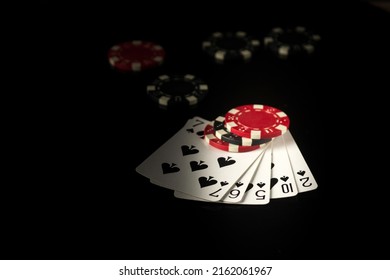 The playing cards on a black table with a straight flush poker winning combination and chips in the background - Shutterstock ID 2162061967