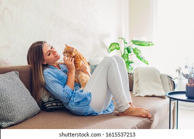 Playing With Cat At Home. Young Woman Sitting And Relaxing On Couch In Living Room And Hugging, Playing With Pet.