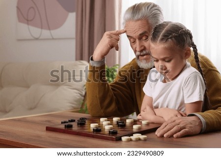 Playing checkers. Grandfather learning little girl at table in room