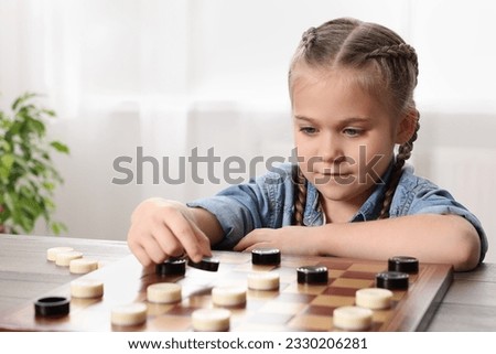 Playing checkers. Little girl thinking about next move at table in room