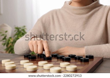 Playing checkers. Woman thinking about next move at table in room, closeup
