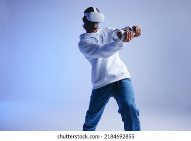 Playing cricket in the metaverse. Sporty young man batting a virtual ball using gaming controllers. Active young man exploring immersive 3D games while wearing virtual reality goggles. - Powered by Shutterstock
