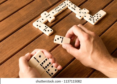 Playing dominoes on a wooden table. Man's hand with dominoes.