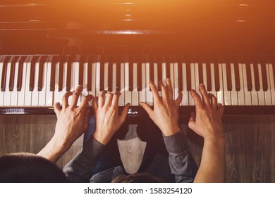 playing four male hands on the piano. palms lie on the keys and play the keyboard instrument in a music school. student learns to play. hands of a pianist. black dark background