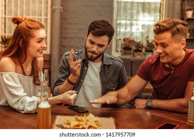 Playing games with friends. Three happy smiling cheerful nice-appealing young-adult attractive friends playing games at the bar while having drinks