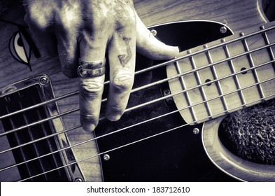 Playing guitar. Tattooed fingers playing bass.