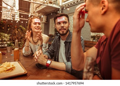 Playing a hedbanz. Happy joyful cheerful attractive smiling glowing young-adult group of friends playing a hedbanz game while sitting at the bar
