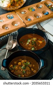 Playing Mancala Board Game While Eating Indian Food Including Chicken Tikka And Pindi Chana Masala As Well As Aloo Matar 