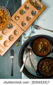 Playing Mancala Board Game While Eating Indian Food Including Chicken Tikka And Pindi Chana Masala As Well As Aloo Matar 