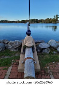 Playing at a nature park on an autumn day. The young boy is sitting on a log that's attached to a cement slab and looking out into the water.