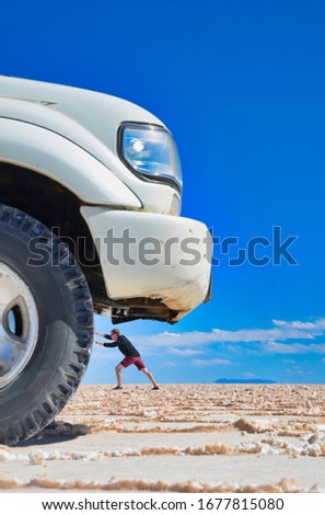 Playing with photography, a car wheel sized man trying to move a giant car, Salar de Uyuni, Bolivia.
