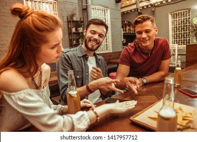 Playing rock-paper-scissors. Three nice-appealing good-looking young-adult friends playing rock-paper-scissors while red-haired beautiful girl feeling upset because of losing