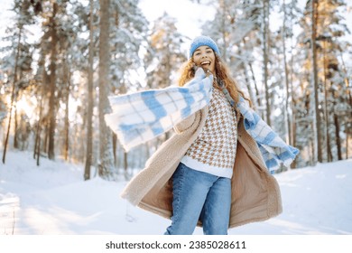 Playing with snow. Beautiful woman in a hat and scarf playing with snow, having fun in a snowy winter forest. Cheerful woman enjoying sunny frosty weather. - Powered by Shutterstock