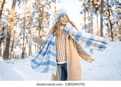 Playing with snow. Beautiful woman in a hat and scarf playing with snow, having fun in a snowy winter forest. Cheerful woman enjoying sunny frosty weather. - Powered by Shutterstock