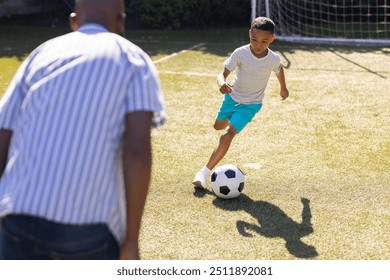 Playing soccer, grandson dribbling ball on field with grandfather watching attentively. sports, mentoring, outdoors, coaching, teamwork, exercise - Powered by Shutterstock