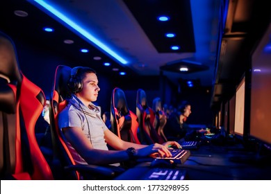 Playing video game on cyber games tournament. Portrait of a teenager with headphones using computer in internet cafe.
