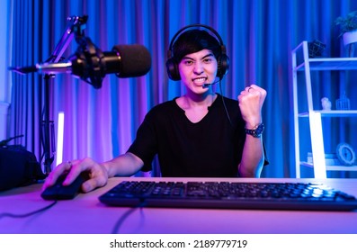 Playing Video Games On Smartphone. Young Asian Handsome Man Sitting On Chair Holding Cellphone In His Hand. Exited Streamer Online Mobile Game In Neon Room .Esport Streaming Game Online.