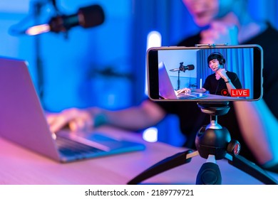 Playing Video Games On Smartphone. Young Asian Handsome Man Sitting On Chair Holding Cellphone In His Hand. Exited Streamer Online Mobile Game In Neon Room .Esport Streaming Game Online.