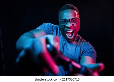 Plays game by using controller. Futuristic neon lighting. Young african american man in the studio. - Powered by Shutterstock