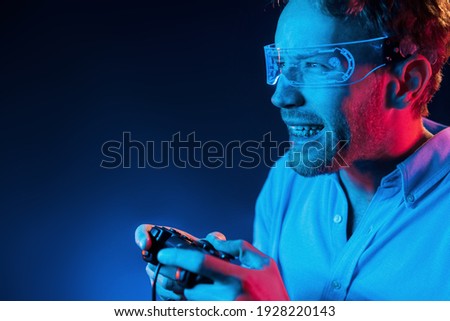 Plays game by using controller. Neon lighting. Young european man is in the dark studio.