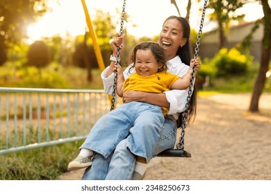 Playtime Moments. Japanese Mom Sitting With Her Toddler Infant Daughter, Swinging Baby And Having Fun on the Playground Outside, Sharing Laughter and Joyful Bonding In Park Outdoors - Powered by Shutterstock