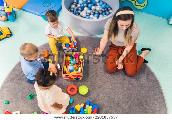 Playtime at nursery school. Toddlers\
with their teacher sitting on the floor and playing with building\
blocks, colorful cars and other toys. High quality\
photo