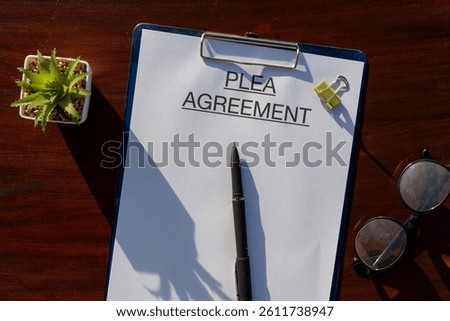 A plea agreement document rests securely inside a clipboard placed on a desk, representing the negotiation process between the defense and prosecution in a criminal case.

