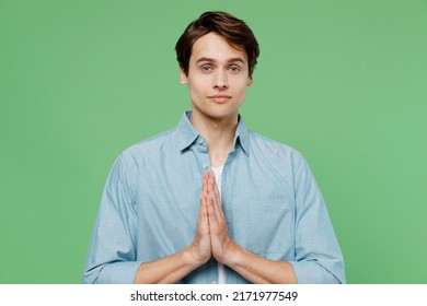 Pleading Jubilant Fancy Delight Young Brunet Man 20s Years Old Wears Blue Shirt Hands Folded In Prayer Gesture Begging About Something Making Wish Isolated On Plain Green Background Studio Portrait