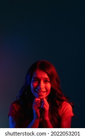 Pleading Woman. Asking Apology. Request Favor. Begging Please. Cute Smiling Young Girl With Imploring Expression In Bright Red Color Neon Light On Dark Copy Space Background.