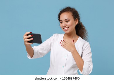 Pleasant African American Doctor Woman Isolated On Blue Background. Doctor In Medical Gown Doing Selfie Shot On Mobile Phone Make Video Call. Healthcare Personnel Medicine Concept. Mock Up Copy Space