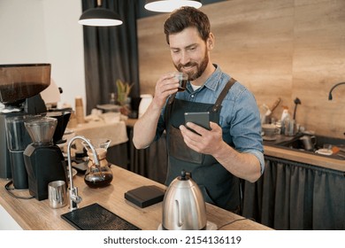 Pleasant Barista Drinking Coffee And Scrolling Through Social Media Feed During Lunch At Workplace