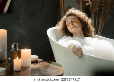 Pleasant caucasian woman puts on eye patches and relaxes in a bubble bath. The woman spends the evening relaxing in the bath and enjoying the aroma of scented candles. - Powered by Shutterstock