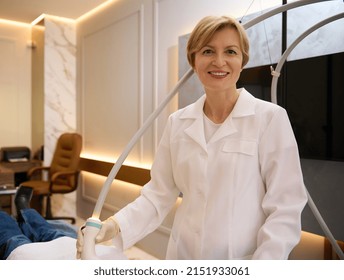 Pleasant Charming Mature Female Aesthetician Smiling Toothy Smile Looking At Camera While Giving Body Care Procedures In Spa Clinic Specializing In Hardware Cosmetology