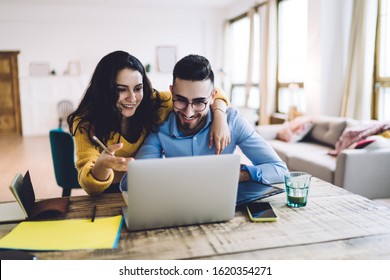Pleasant cheerful female with pencil in hand helping handsome busy male with telemediated work, browsing laptop and smiling at home 