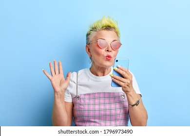 Pleasant Funny Old Lady Blowing Kiss To Her Lover While Talking With Him By Mobile Phone. Flirt Concept. Love. Isolated Blue Background