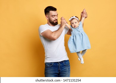 pleasant man holding his baby and teaching her to dance, first experience. close up photo. isolated yellow background. studio shot.