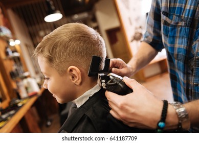 Pleasant professional barber using haircutting machine