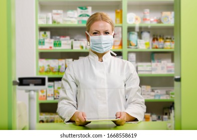 Pleasant professional young female pharmacist with surgical mask smiling 