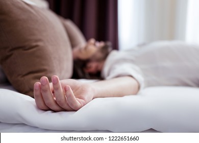 Pleasant rest. Selective focus of a hand of a handsome relaxed man lying on the bed