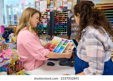 Pleasant saleswoman holding palette with color swatches of watercolor paints of various spectrums, demonstrating it to customer shopping in a stationery store. Creative hobby. Art. Painting. Business - Powered by Shutterstock