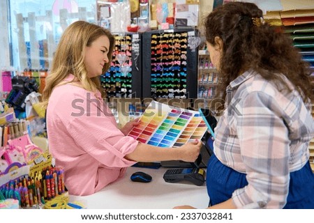 Pleasant saleswoman holding palette with color swatches of watercolor paints of various spectrums, demonstrating it to customer shopping in a stationery store. Creative hobby. Art. Painting. Business