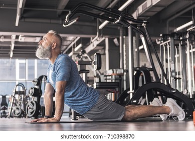 Pleasant Senior Male Is Enjoying Yoga In Fitness Center