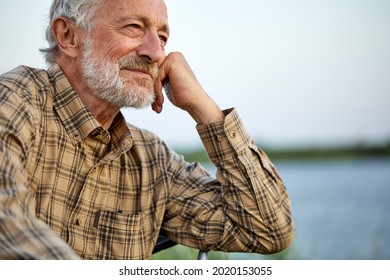 Pleasant Senior Man In Checkered Shirt Sit On Chair In Nature, Having Rest Alone, Thinking, Smiling, In Contemplation Of Countryside Landscapes, Portrait Of Gray Bearded Male Relaxed