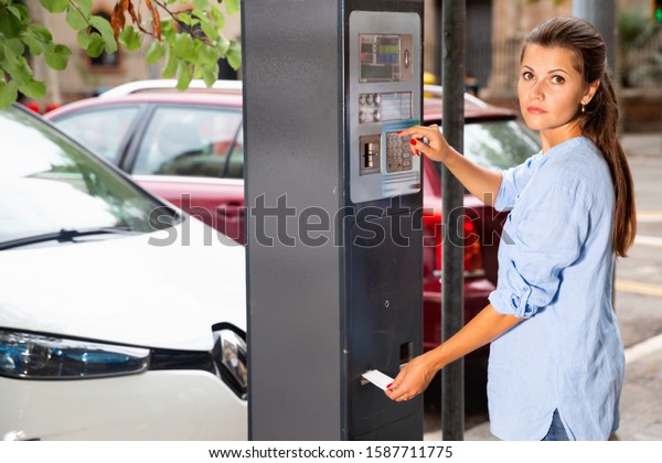 Pleasant serious  woman paying for parking in\
modern parking meter on city\
street