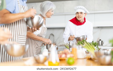 Pleasant and sociable young man, professional chef, leading culinary courses, imparting cooking skills to diverse group of people of different ages - Powered by Shutterstock