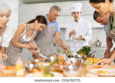 Pleasant and sociable young man, professional chef, leading culinary courses, imparting cooking skills to diverse group of people of different ages - Powered by Shutterstock