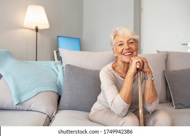 Pleasant thoughtful aged woman seating with a walking stick. Retired woman with her wooden walking stick at home. Happy senior woman relaxing at home holding cane and looking at camera. - Powered by Shutterstock